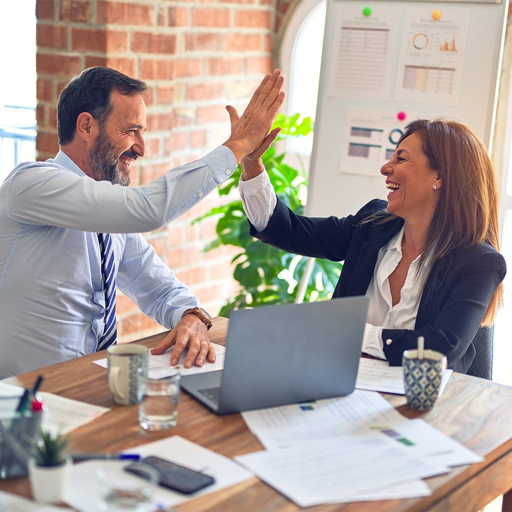 A smiling man and woman high-five across a desk with a laptop